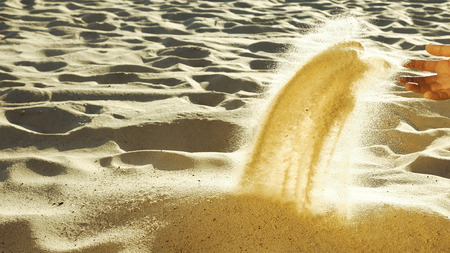 Man sieving sand with his hand. Barefoot human playing in desert. Senseless act and loneliness concept. Close-up. Side view.の写真素材