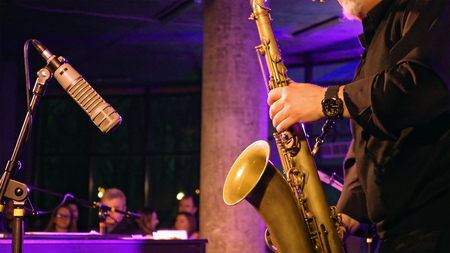 Saxophone player plays the saxophone on the stage with microphone. Jazz retro vintage concert performance entertainment. Close up shot with selective focus.