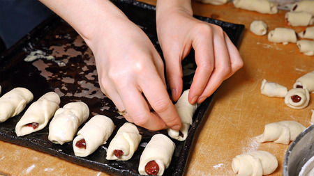 Baker puts raw homemade croissants on the oven baking tray pan