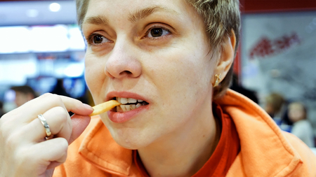 Young woman eats fast food french fries in cafe restaurantの写真素材