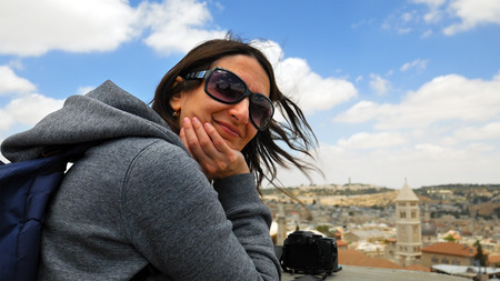 Longhair woman enjoys the Jerusalem cityscape outdoors in windy weather. Her hair is waving and...