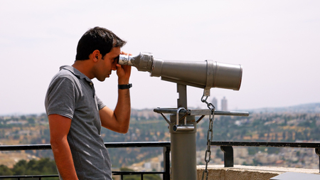 Jerusalem, Israel - May 25, 2017: Tourist looks in binoculars tower viewer at the city view. Tower viewer is popular device to look at the city details. Tourists love to use binoculars.のeditorial素材