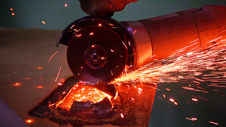 Cutting metal with disc grinder abrasive saw producing bright colorful sparks. Worker cuts metal with hand electric tool.の写真素材