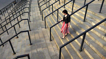Beautiful brunette woman in red striped pleated skirt is running downstairs. City life urban people behavior. The skirt and her hair are fluttering in the wind. High angle overhead.の写真素材