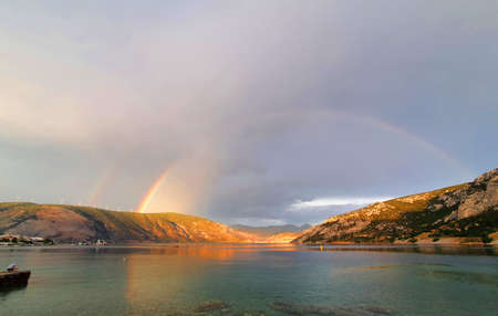 Rainbow over the sea and mountainsの写真素材