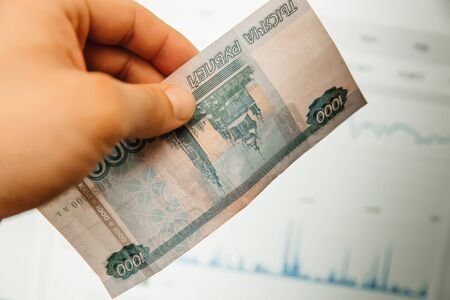 A hand holds Russian banknotes against the background of trading charts. The concept of exchange ratesの写真素材
