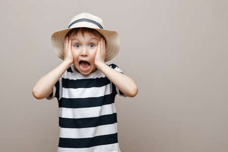 Portrait of a surprised cute baby boy standing isolated on a gray background. I look at the camera. hands near the open mouth showing a true surprised reaction to unexpected newsの写真素材