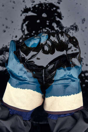 Rubber gloves soaked in oil on the background of spilled oil. Crisis of the oil industry. Economic downturn. Black gold.の写真素材