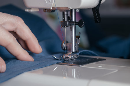 Close-up of the hands of the girl seamstress behind the workplace, sewing clothes in the sewing...
