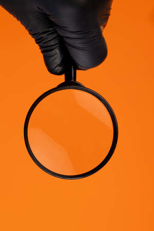 Magnifier on an orange background. A hand with a magnifying glass on an isolated background. Vertical. Copy spaceの写真素材