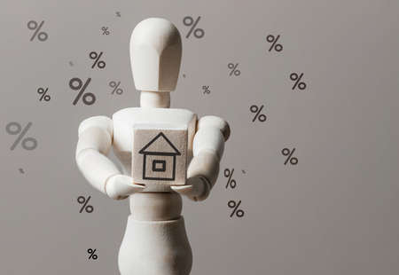 Wooden figure of a man holds a house in his hands and interest is flying around. Concept of discounts on real estate. Copy spaceの写真素材