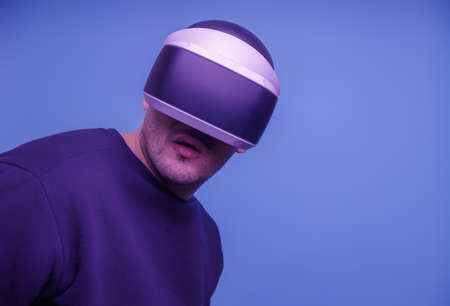 Young handsome bearded man in his thirties wearing virtual reality glasses in a studio on a blu...