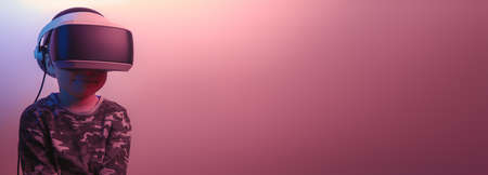 Five-year-old child in a camouflage T-shirt poses with virtual reality glasses in front of the studio. Copy spaceの写真素材