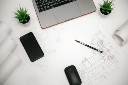 Laptop, phone and rolls of drawings on the Desk in engineering. architectural background with rolls of technical drawings