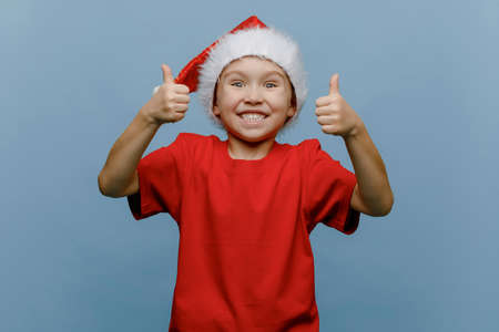 image of a joyful Caucasian boy in a Christmas hat, gesturing with a CLASS sign, is highlighted on a blue backgroundの写真素材