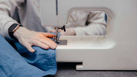 seamstress girl works, sews clothes on a sewing machine, hands close-up. The process of sewing in an atelier or workshop. Tailoring and repair of clothing. Self-employed employee.の写真素材
