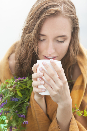 Freezing and wet woman in plaid enjoying tea with herbsの写真素材