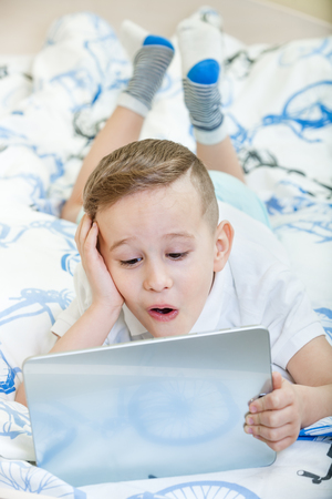 Adorable kid with tablet pc lying on the bedの写真素材