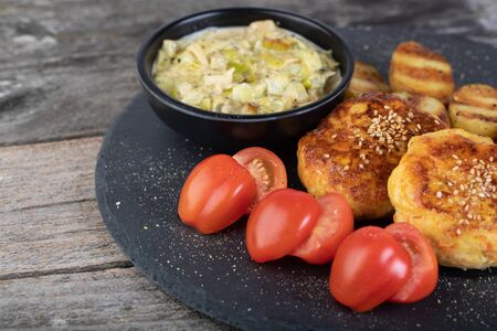 Lunch of fish cutlet with baby potatoes and leek sauce served on a black stone plateの写真素材