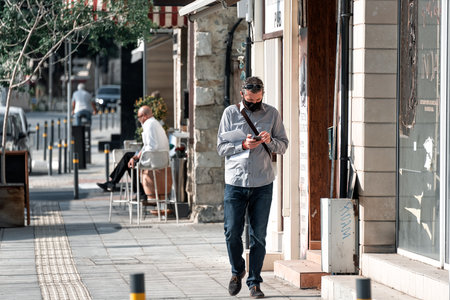 Limassol, Cyprus - November 10, 2020: Man walking down a sunny street wearing a face mask during Covid-19 pandemicのeditorial素材