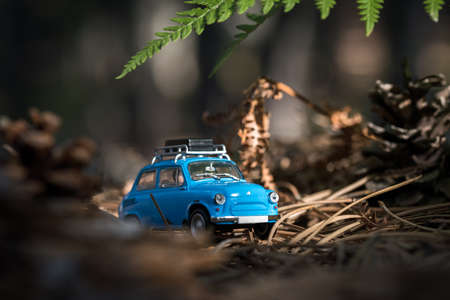 Cute little nonexistent retro car with luggage on top on a forest roadの写真素材
