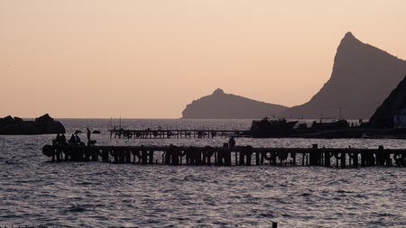 Fishermen sit on the dock and catch fish at sunsetの写真素材