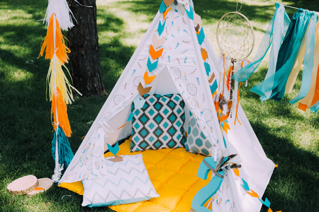 Holiday design for children's holiday in boho style, a magical children's birthday party. Design frame with bird feathers in turquoise, beautiful Indian hut with beautiful cushions and printsの写真素材