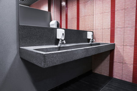 Modern granite washbasin for public restroom with hot and cold water, against tile background. High quality photoの写真素材
