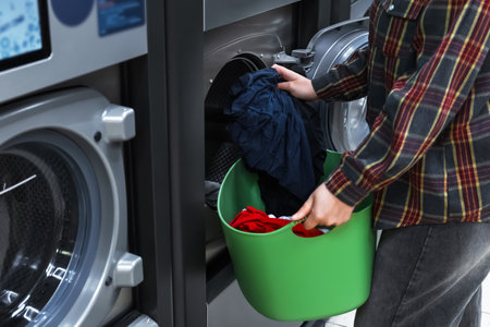 A girl loads colorful laundry into a self-service washing machine.の写真素材