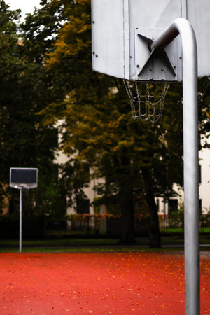 An outdoor basketball court on an autumn day. The court features a red surface, surrounded by trees with yellow and orange leaves. Two basketball hoops are visible.の写真素材