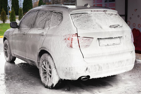 A car covered in foam at a self-service car wash. The vehicle is parked under a wash station, showcasing a clean and shiny exterior.の写真素材