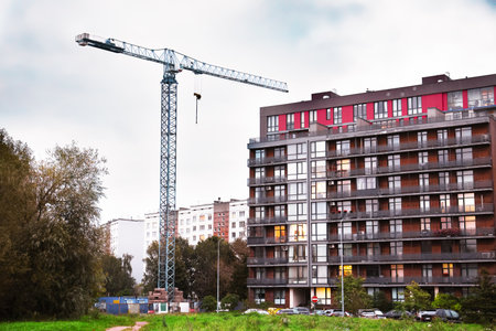 Tower crane at a construction site for a new residential building. Nearby completed houses and a clear blue sky in the background during autumn.の写真素材