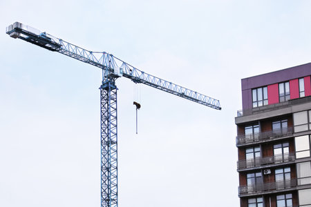 Tower crane at a construction site for a new residential building. Completed houses and a clear blue sky are visible in the background during autumn.の写真素材