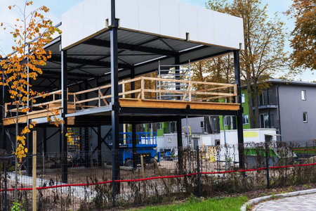 A truck crane operates at a construction site surrounded by fencing. A new building structure is visible with a foot lift and construction materials nearby.の写真素材