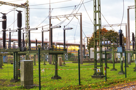 An electrical substation with various power equipment, including transformers and wires, surrounded by a fence and green grass.の写真素材