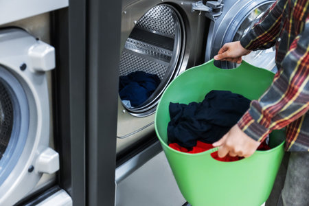 A girl loads colorful laundry into a self-service washing machine.の写真素材