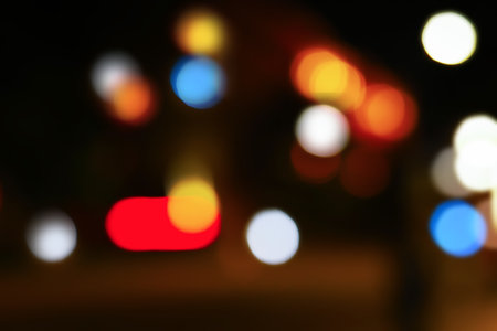 Blurred lights illuminate a night city scene at a bus stop. Various colors create a vibrant atmosphere, suggesting urban life and movement.の写真素材