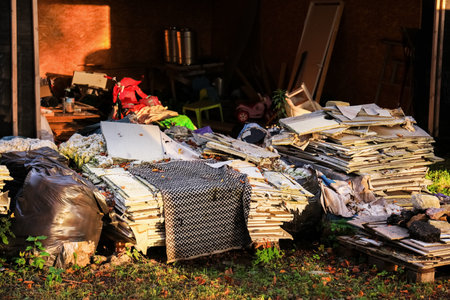 A cluttered outdoor area filled with piles of discarded materials, including cardboard, plastic bags, and various debris. Sunlight casts shadows on the mess.の写真素材