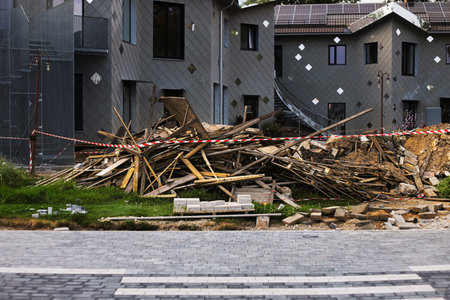 Construction waste piles up near newly built modern buildings. The scene shows debris, wooden planks, and a paved road in an urban setting.の写真素材