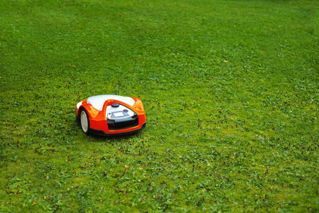 A robotic lawn mower operates on a lush green lawn. The mower is compact with a white and orange design, efficiently cutting grass in a residential setting.の写真素材