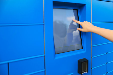 A blue parcel machine designed for receiving packages. A hand is interacting with the touchscreen interface. The machine features multiple compartments for parcel storage.の写真素材