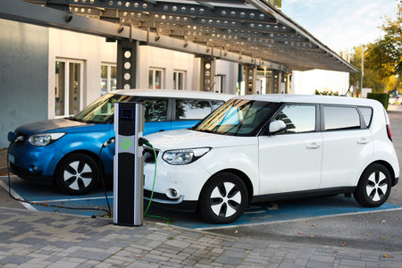 A white electric car is charging at a station in a parking lot designed for electric vehicles. A...
