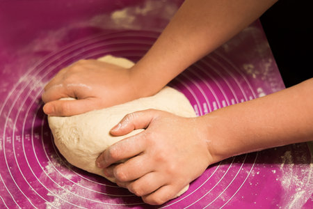 A close-up of hands firmly pressing and kneading a fresh ball of dough on a pink, flour-dusted silicone baking mat. High quality photoの写真素材