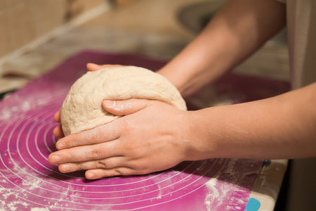 A close-up shot of hands gently holding and shaping a ball of dough on a flour-dusted, pink silicone...