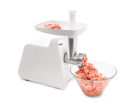 A white electric meat grinder with a white plunger, mincing raw pink meat chunks into a heap of ground meat in a glass bowl. High quality photoの写真素材