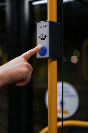 A young woman presses the stop button on a modern city bus. Yellow posts are installed inside, providing a clear view of the interior. High quality photoの写真素材