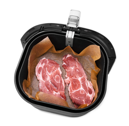 An overhead view of two raw pork neck steaks on parchment paper inside the opened basket of a black and white air fryer. High quality photoの写真素材