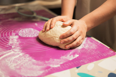 A close-up of hands firmly rolling and shaping a fresh ball of dough on a pink, flour-dusted silicone baking mat. High quality photoの写真素材