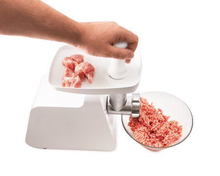 A white electric meat grinder with a white plastic plunger, mincing raw pork chunks into a clear glass bowl on white. High quality photoの写真素材