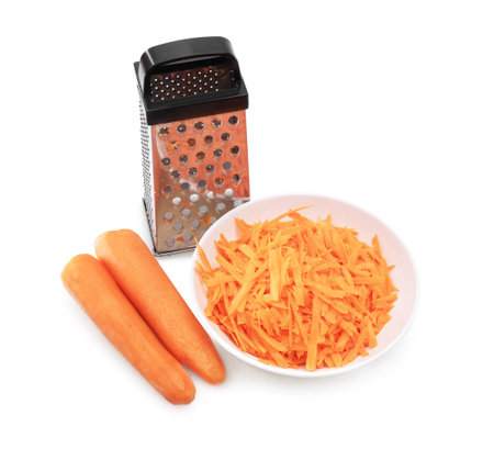 Two peeled carrots, a metal box grater, and a white bowl of shredded carrots, forming an isolated composition on a white background. High quality photoの写真素材